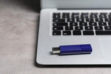 Photo of Usb flash drive and laptop on light grey table, closeup. Space for text