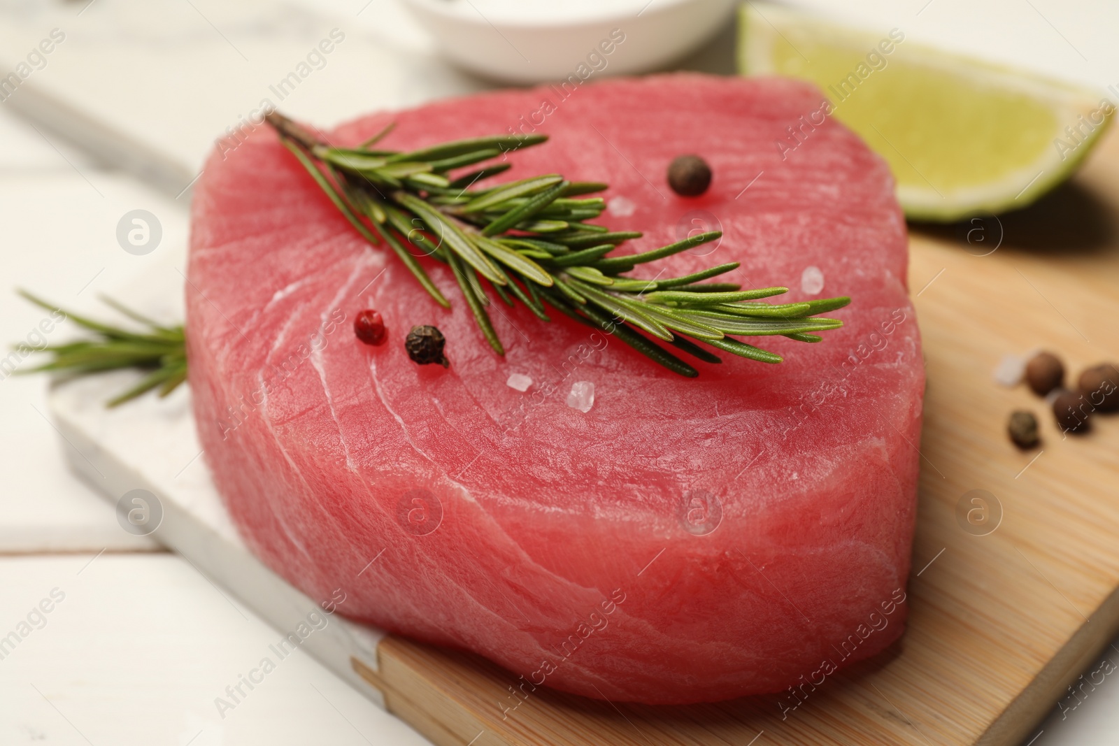 Photo of Raw tuna fillet with rosemary and spices on white table, closeup
