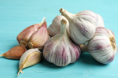 Photo of Fresh unpeeled garlic bulbs and cloves on light blue wooden table, closeup. Organic product