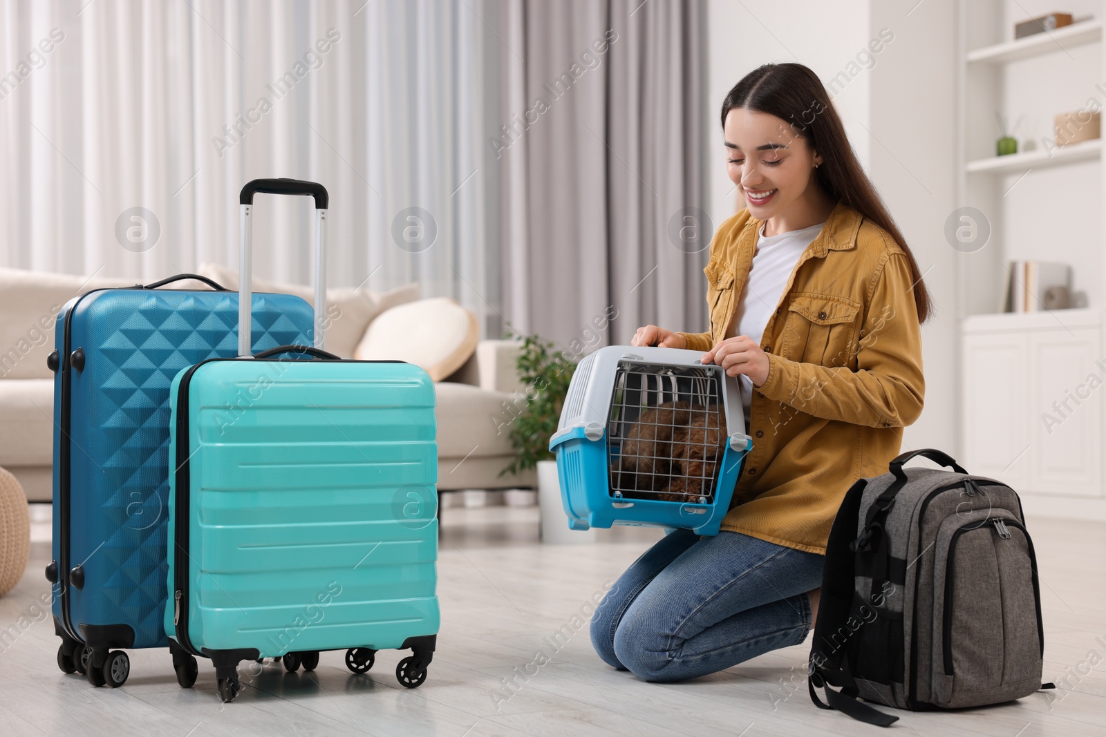 Photo of Travelling with pet. Smiling woman looking at carrier with her dog indoors