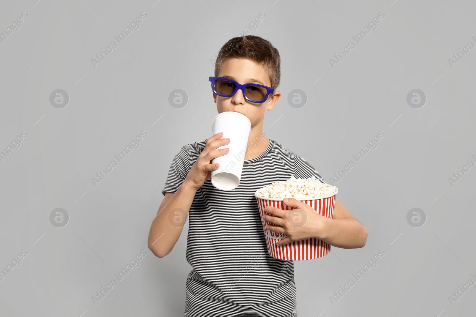 Photo of Boy with 3D glasses, popcorn and beverage during cinema show on grey background