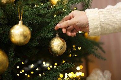 Photo of Woman decorating fir tree with golden Christmas ball indoors, closeup