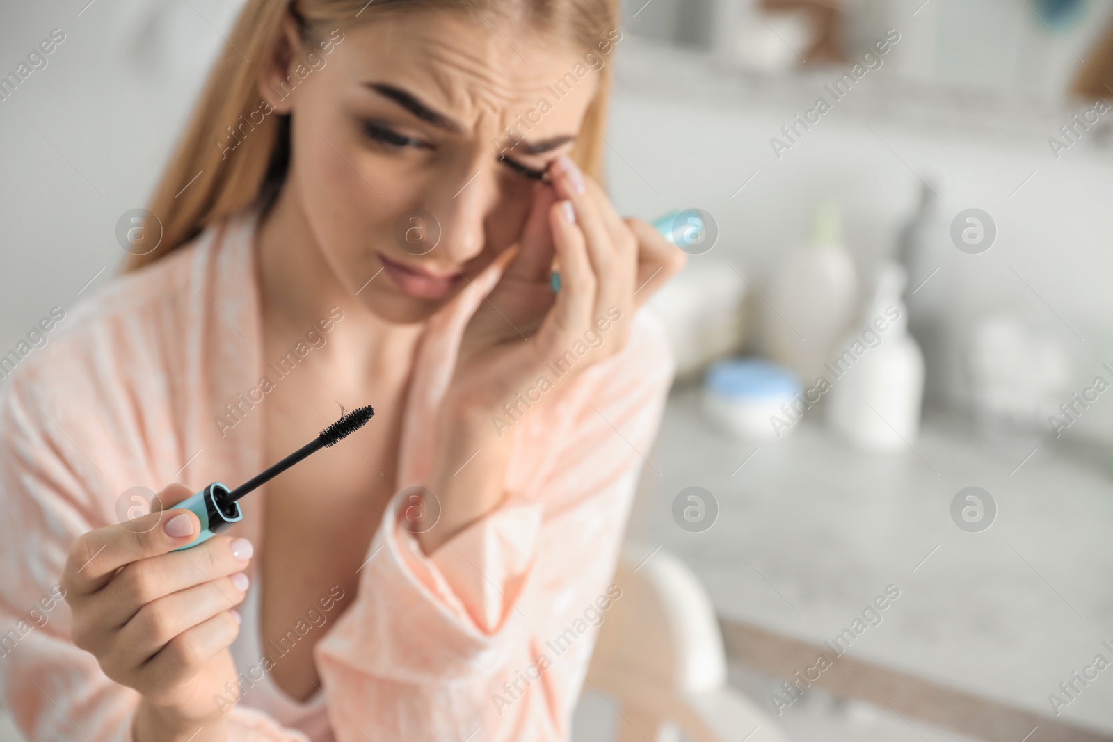 Photo of Young woman holding mascara brush with fallen eyelashes indoors