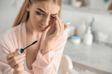 Young woman holding mascara brush with fallen eyelashes indoors