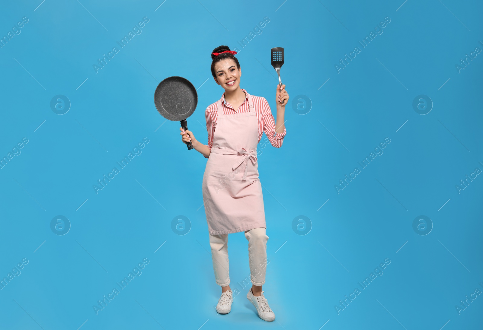 Photo of Housewife with frying pan and spatula on light blue background