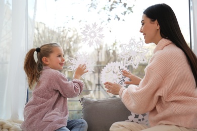 Mother and daughter decorating window with paper snowflakes at home