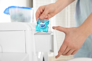 Photo of Woman putting laundry detergent capsule into washing machine, closeup