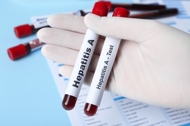 Scientist holding tubes with blood samples for hepatitis virus test near laboratory form, closeup