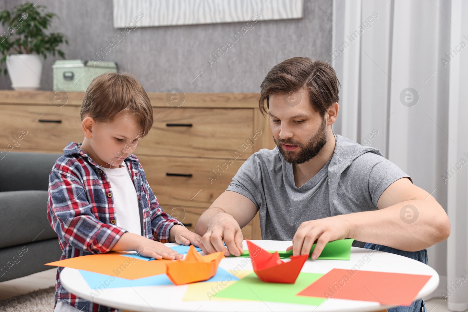 Photo of Dad and son making paper boats at coffee table indoors