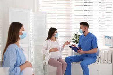 Photo of Doctor consulting patient while other pregnant woman waiting for appointment in clinic