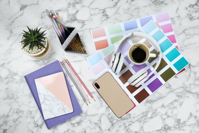 Photo of Flat lay composition with phone, notebook and color palettes on white marble table. Designer's workplace