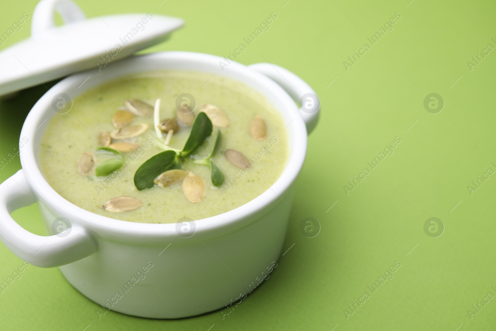 Photo of Delicious broccoli cream soup with pumpkin seeds on green background, closeup. Space for text