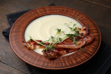 Delicious potato soup with bacon and microgreens in bowl on wooden table, closeup