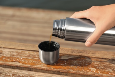 Photo of Woman pouring hot drink from thermos into cap outdoors, closeup