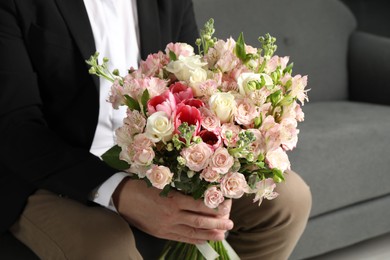 Photo of Man with beautiful bouquet of flowers on sofa indoors, closeup