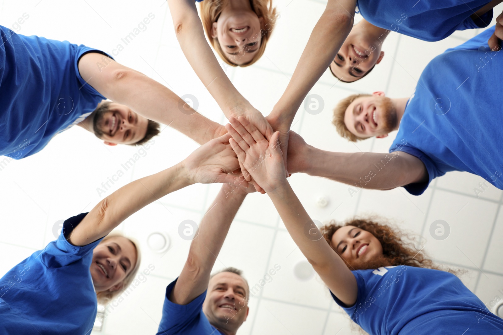 Photo of Team of volunteers putting their hands together on light background, bottom view