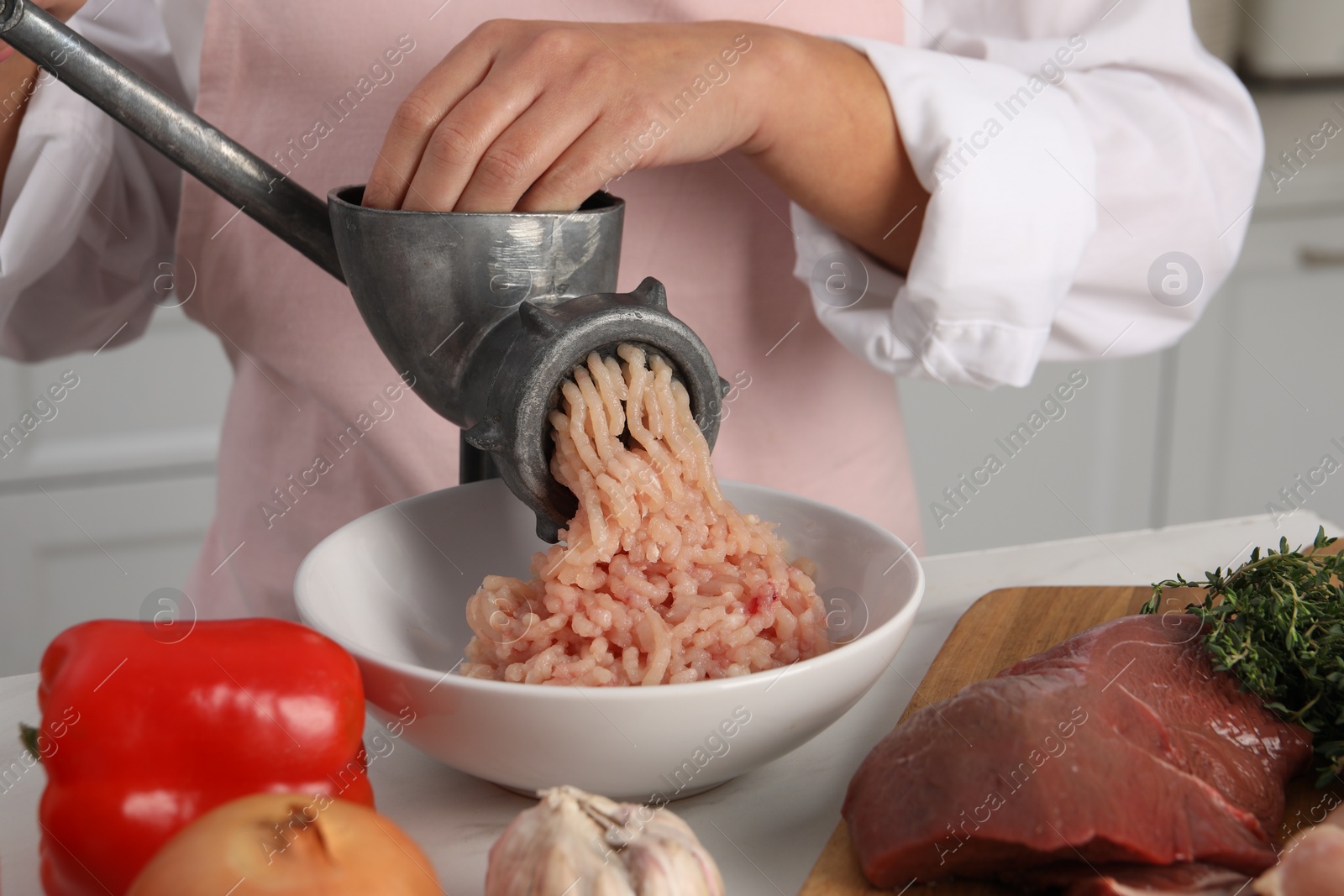 Photo of Woman making chicken mince with metal meat grinder at white table in kitchen, closeup
