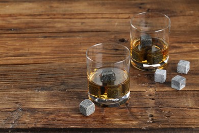 Photo of Whiskey stones and drink in glasses on wooden table. Space for text