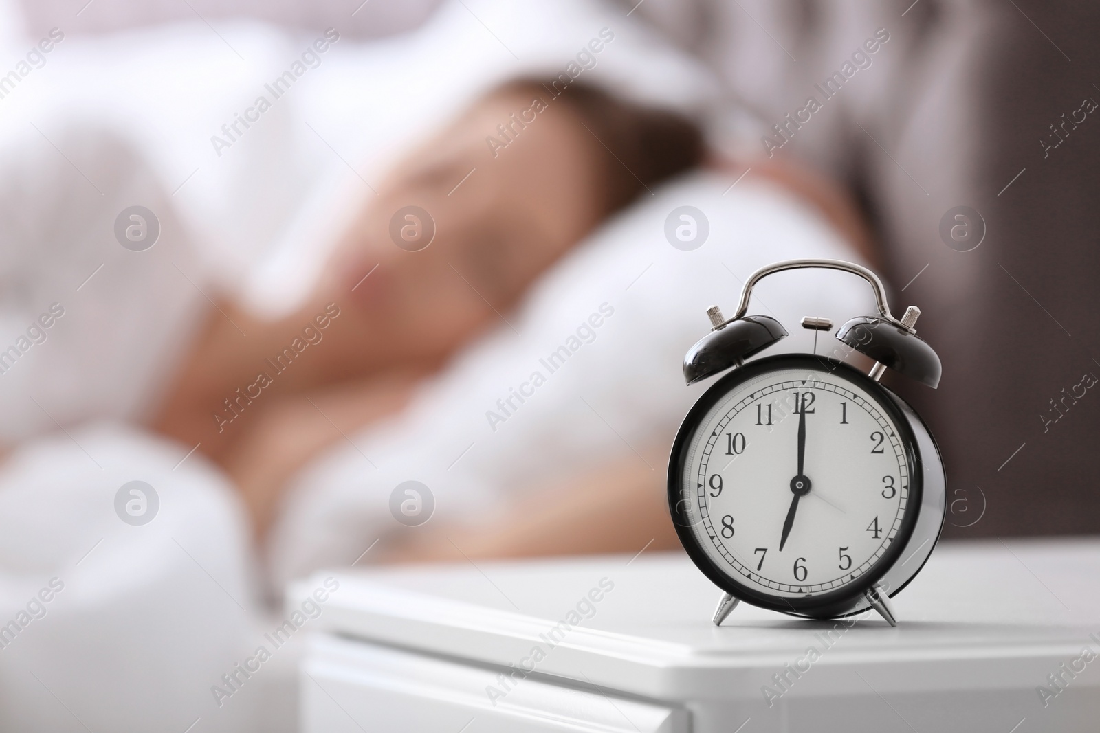 Photo of Alarm clock on table and woman in bedroom. Sleeping time