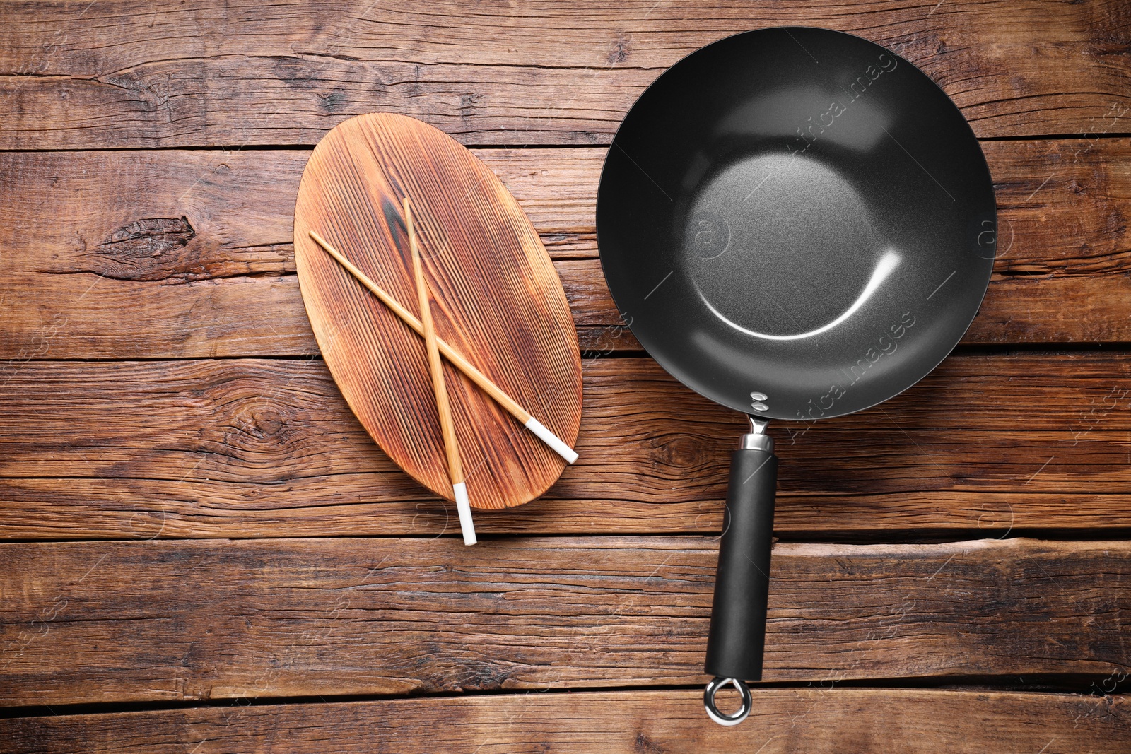 Photo of Empty iron wok and chopsticks on wooden table, flat lay