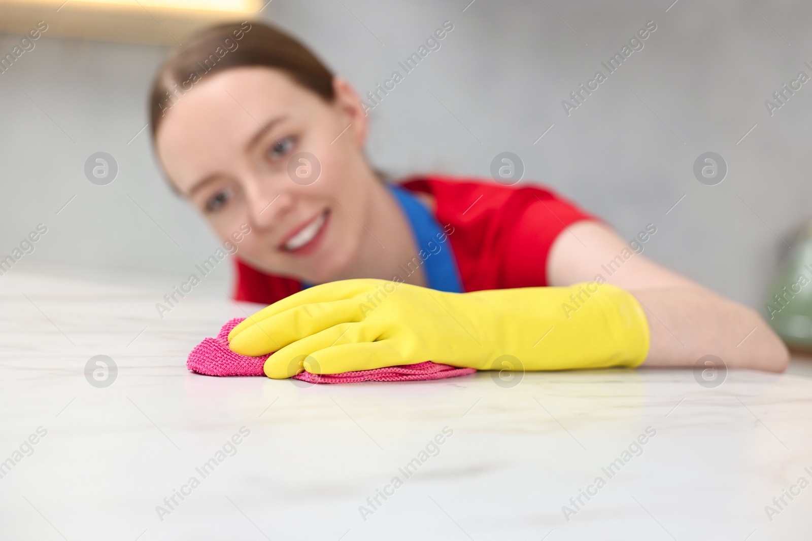 Photo of Woman cleaning white marble table with rag in kitchen, selective focus