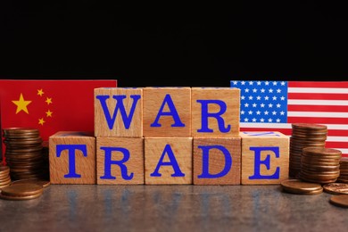 Words War Trade made of wooden cubes, American and Chinese flags with coins on grey table against black background