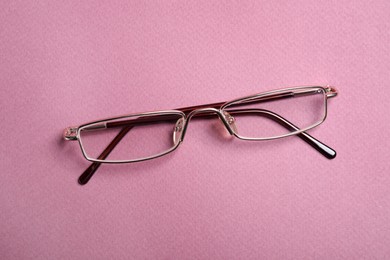 Photo of Stylish pair of glasses with metal frame on pink background, top view