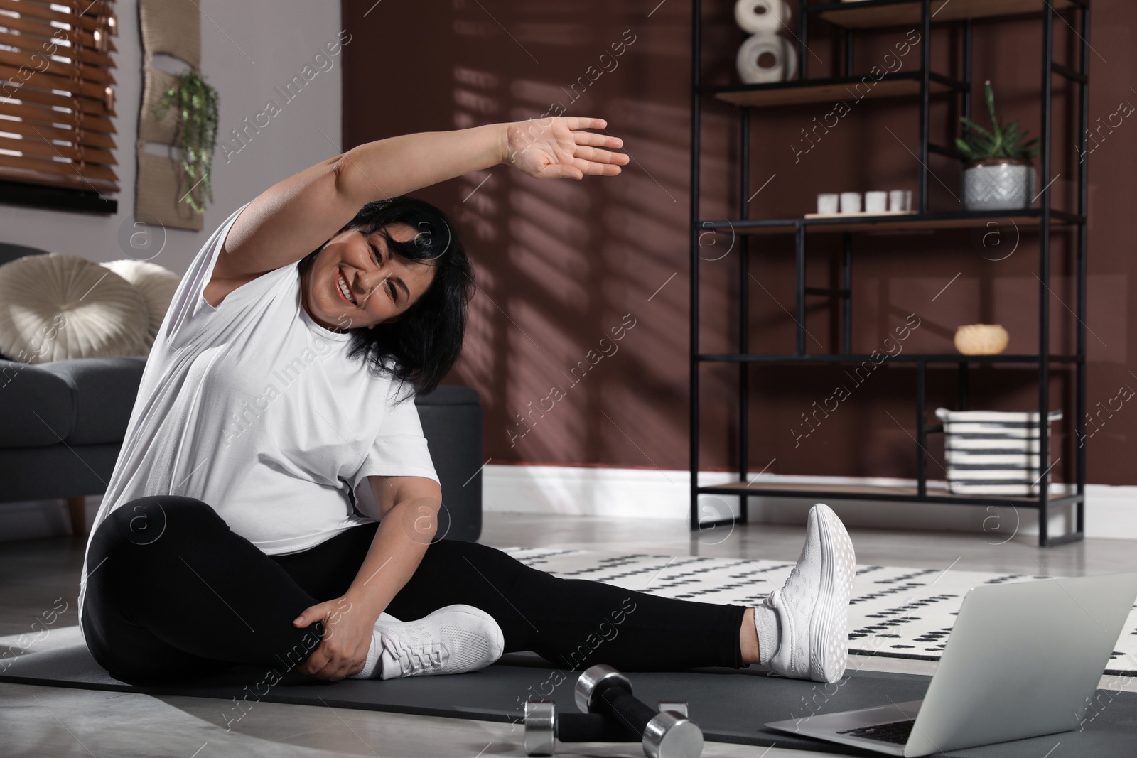 Photo of Overweight mature woman stretching while watching online class at home