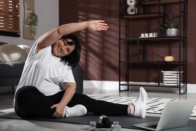 Overweight mature woman stretching while watching online class at home