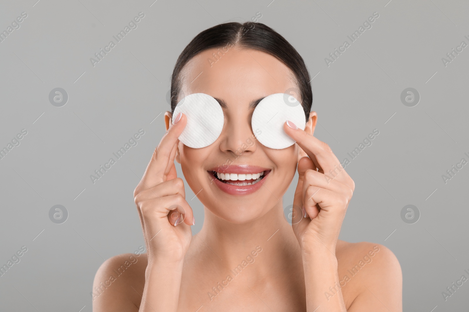 Photo of Beautiful woman removing makeup with cotton pads on light grey background