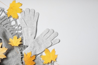 Photo of Stylish woolen gloves, scarf and dry leaves on white background, top view