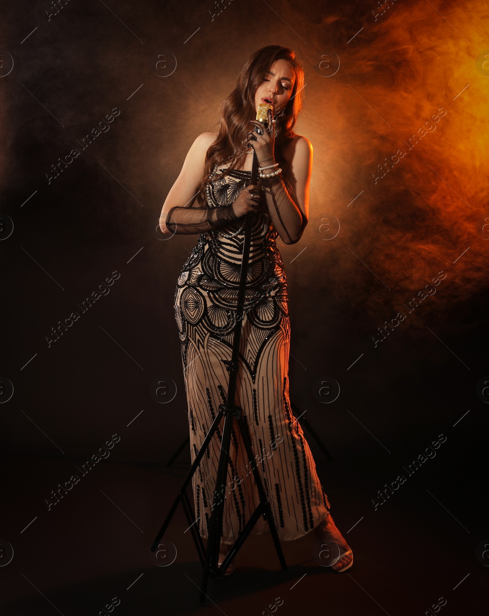 Photo of Beautiful young woman with microphone singing in color lights and smoke