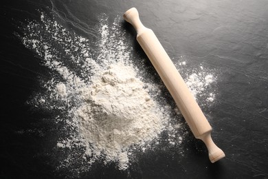 Photo of Pile of flour and rolling pin on black textured table, top view