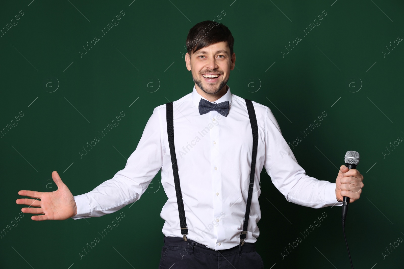 Photo of Handsome man in formal clothes posing with microphone on color background