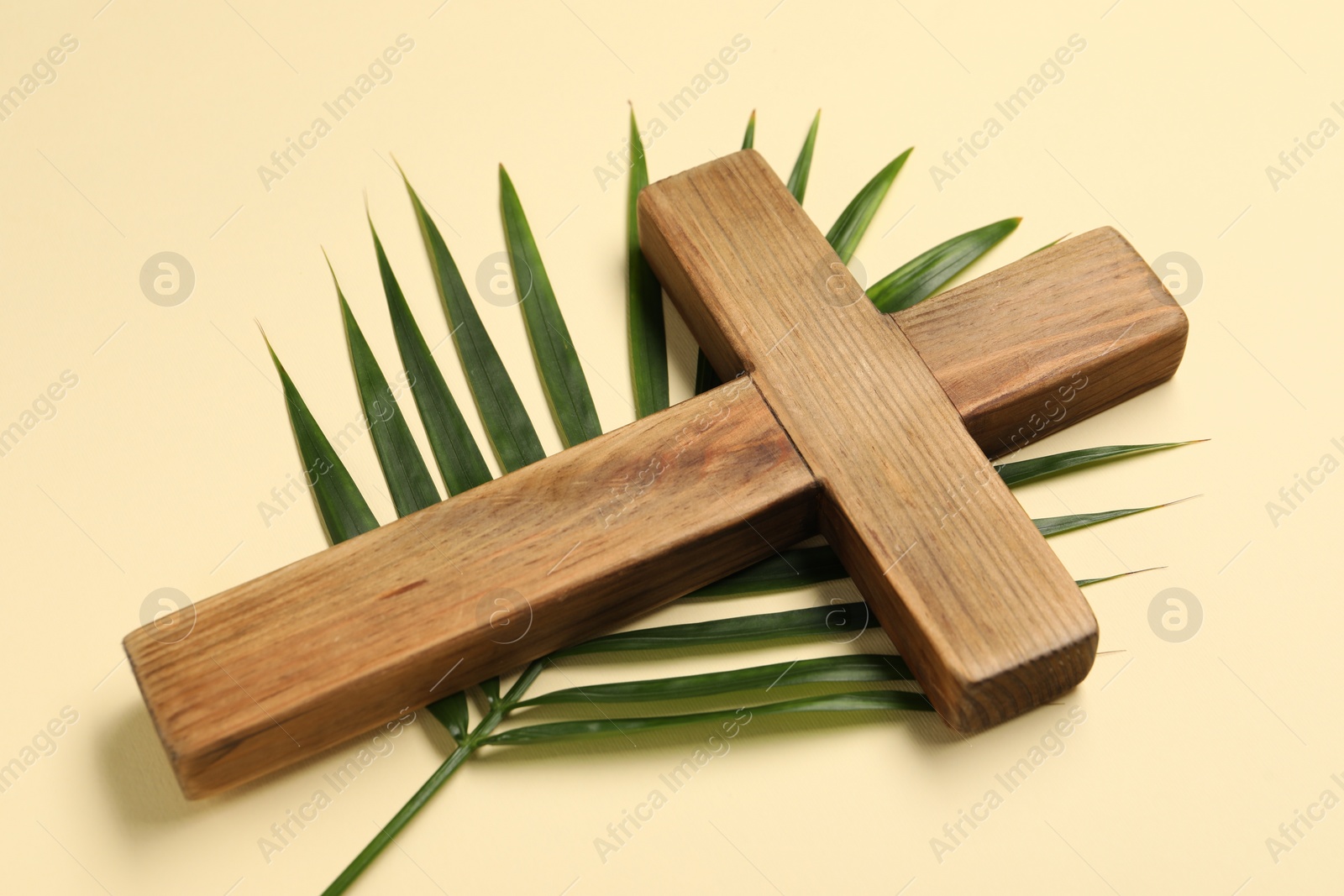 Photo of Wooden cross and palm leaf on beige background. Easter attributes