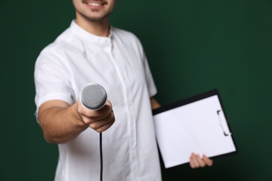 Young man in casual clothes holding microphone and clipboard on color background. Space for text