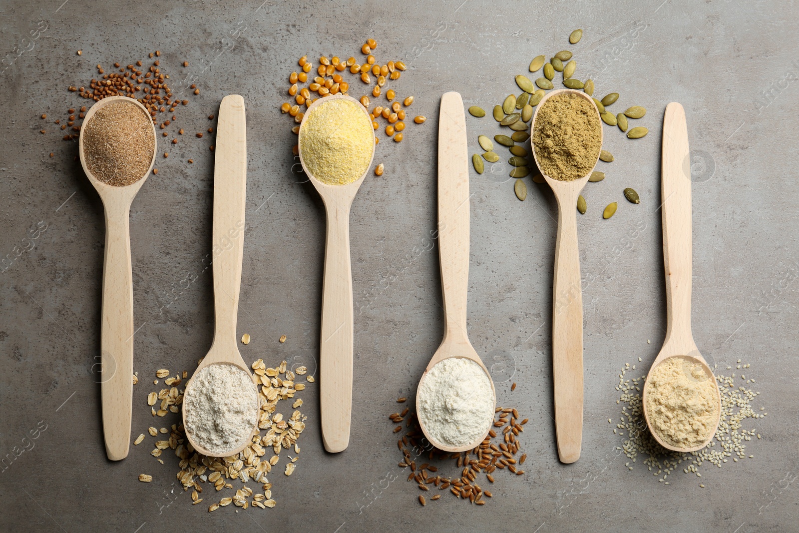 Photo of Spoons with different types of flour and ingredients on grey table, top view