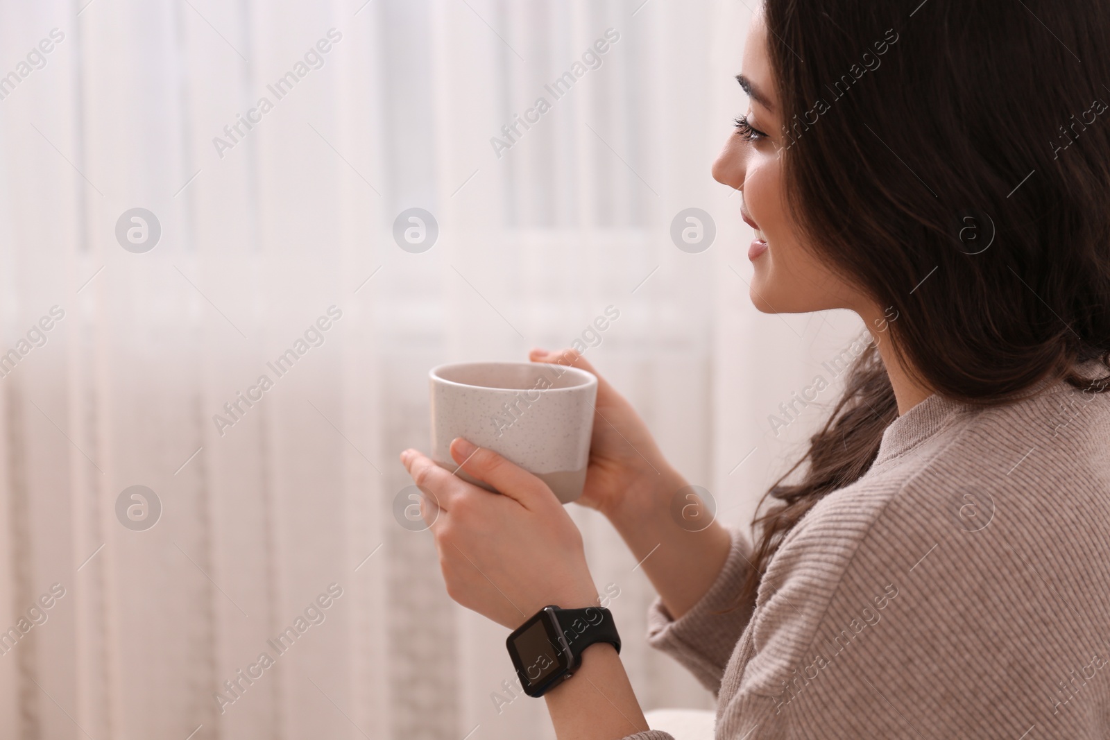 Photo of Young woman with smart watch and cup of drink at home, space for text