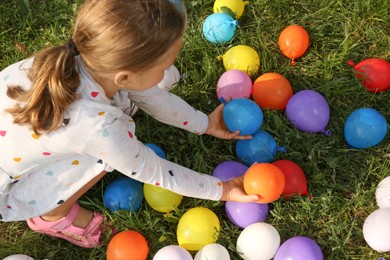 Little girl with water bombs on green grass, above view