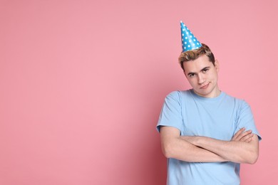 Sad young man with party hat on pink background, space for text