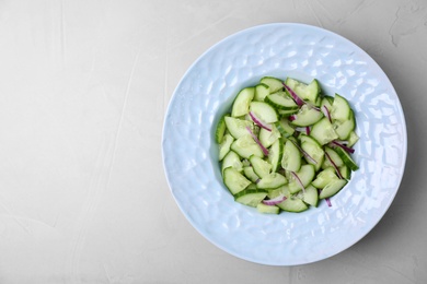 Plate of vegetarian salad with cucumber and onion served on light background, top view