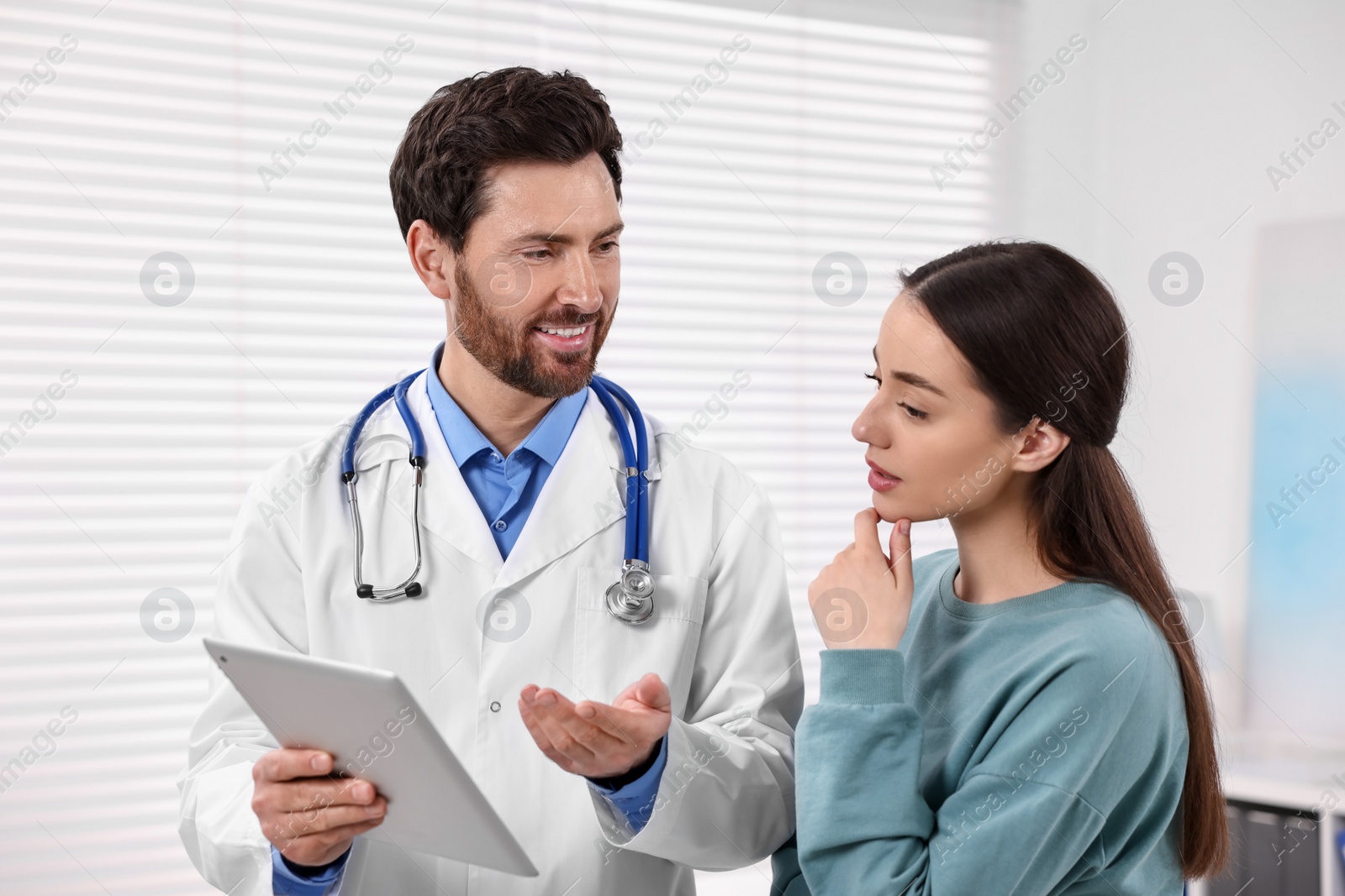 Photo of Doctor with tablet consulting patient during appointment in clinic