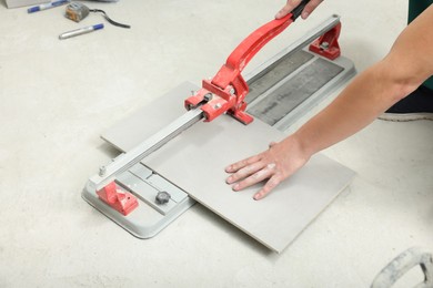 Photo of Worker using manual tile cutter indoors, closeup