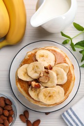 Photo of Tasty pancakes with sliced banana served on white wooden table, flat lay