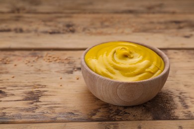 Photo of Sauce bowl with delicious mustard on wooden table. Space for text