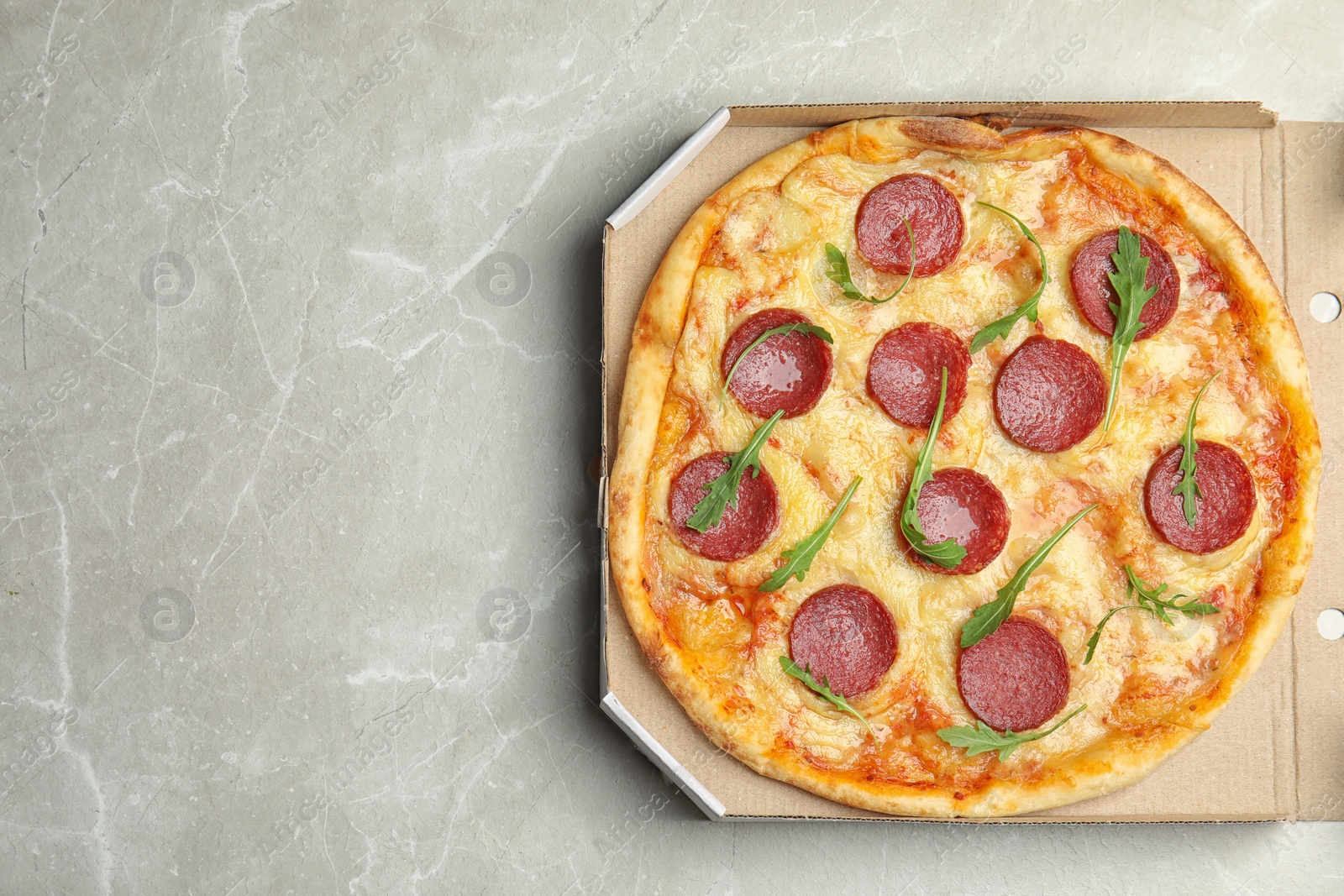 Photo of Tasty pepperoni pizza in cardboard box on light grey marble table, top view. Space for text