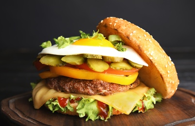 Tasty burger with fried egg on board against dark background