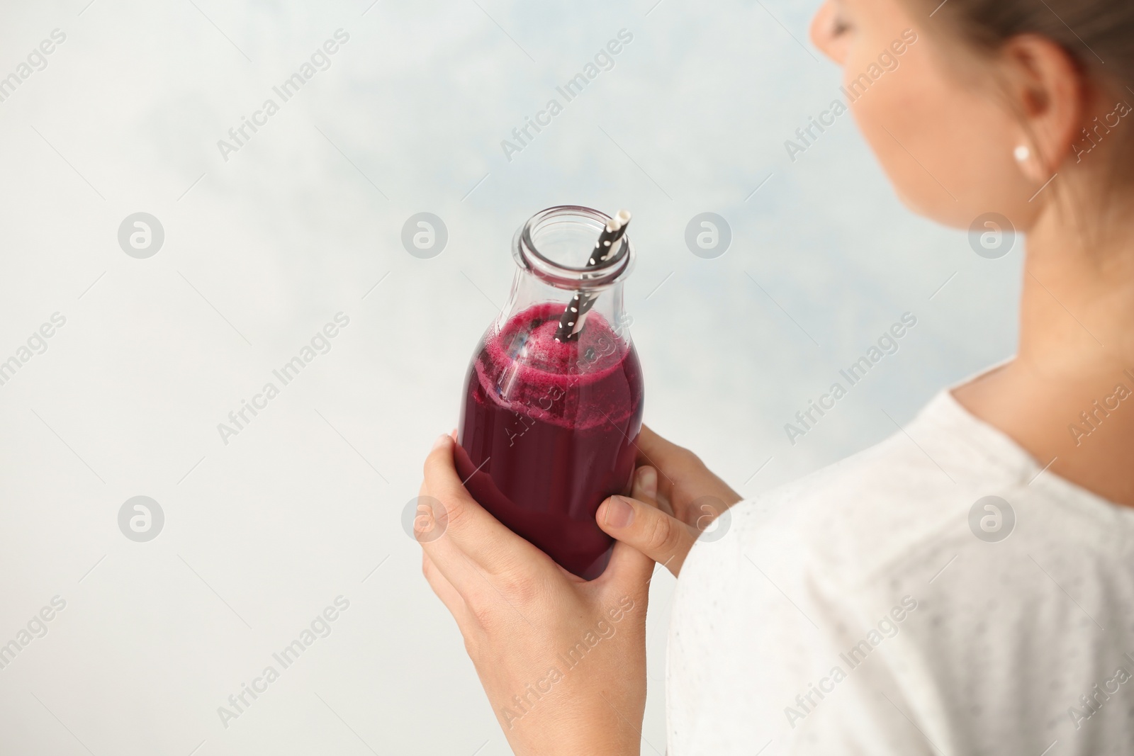 Photo of Woman holding bottle of beet smoothie on light background with space for text, closeup