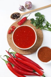 Photo of Spicy chili sauce in bowl and ingredients on white background, flat lay