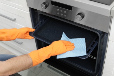 Young man cleaning oven tray with rag in kitchen, closeup